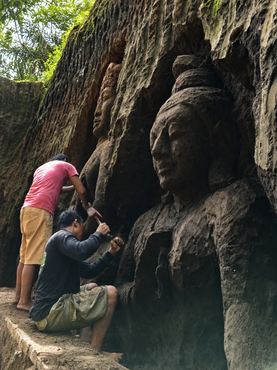 Artisans carving monumental faces directly into a volcanic rock wall